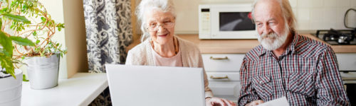 Senior couple enjoying their time together at home with a laptop and paperwork, sharing a moment of connection and possibly managing household affairs, while staying vigilant about senior identity theft.