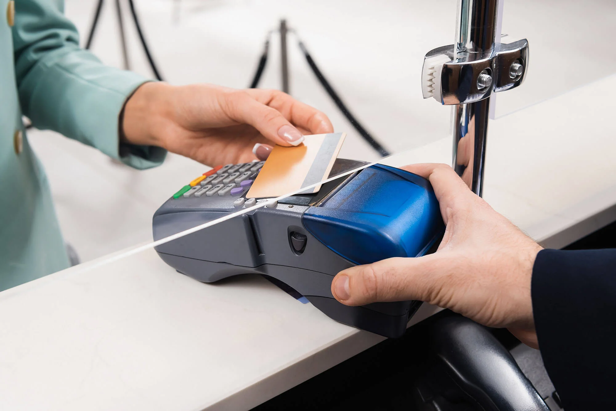 A customer is tapping a contactless credit card on a point-of-sale terminal while a salesperson assists with the transaction.