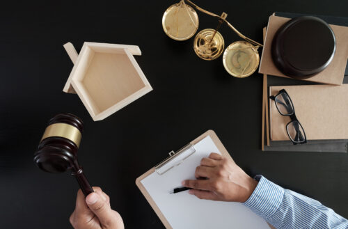 A person's hand holding a gavel with legal documents and scales of justice on a desk, symbolizing legal proceedings or the work of a judge or law practitioner, potentially highlighting issues of inaccurate reporting.