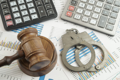 A wooden judge's gavel, metal handcuffs, calculators, and financial charts spread out on a surface, symbolizing the intersection of law, crime, and fraudulent credit finance.