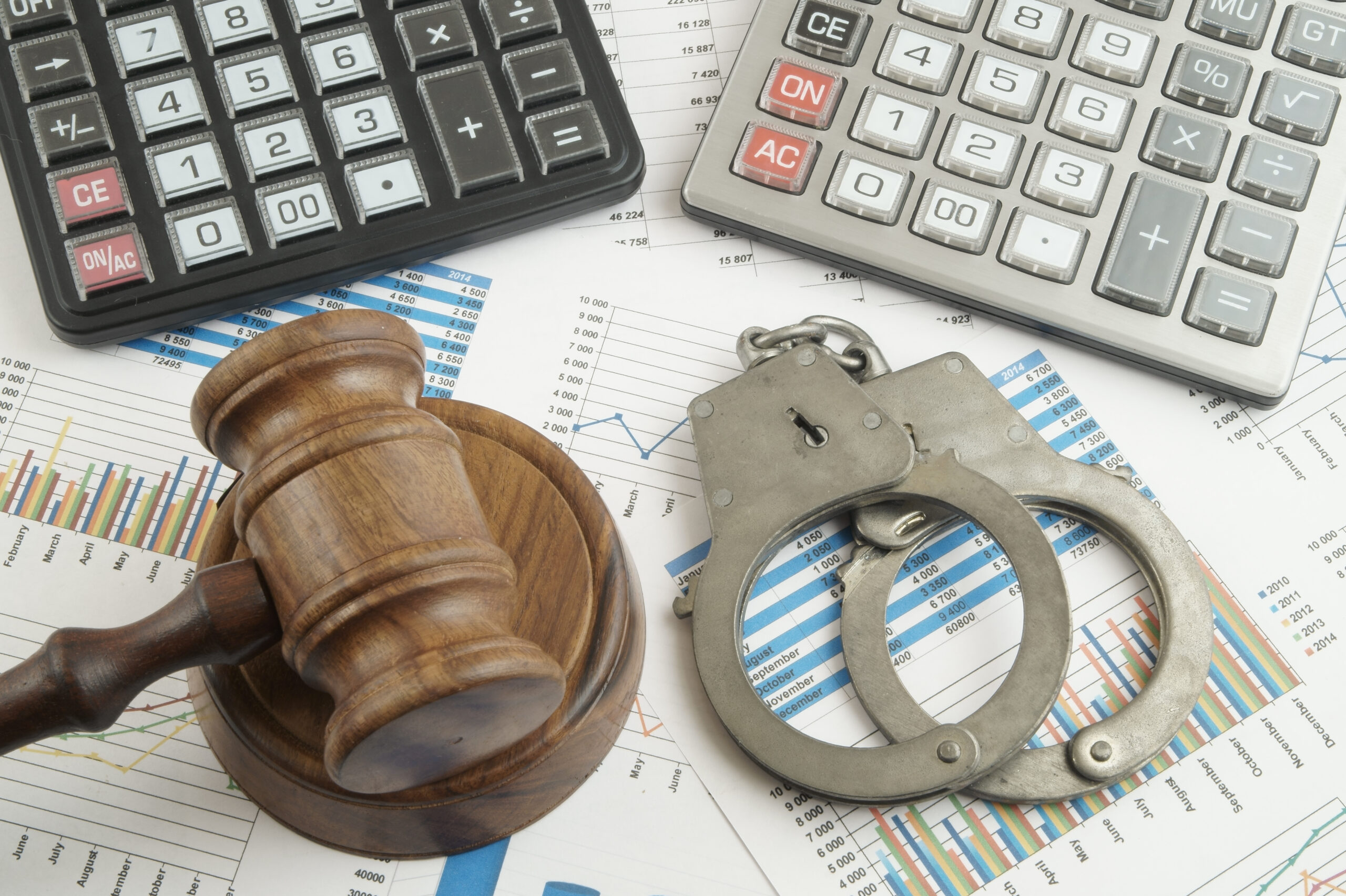 A wooden judge's gavel, metal handcuffs, calculators, and financial charts spread out on a surface, symbolizing the intersection of law, crime, and fraudulent credit finance.
