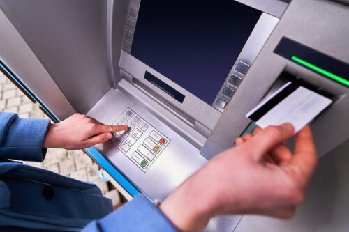 A person in a blue jacket using an unauthorized atm, entering their pin while withdrawing or depositing money.