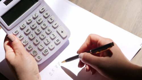 person holding calculator and writing numbers