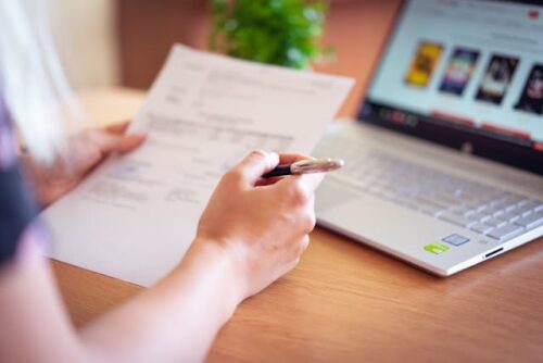 person looking at paper document near computer