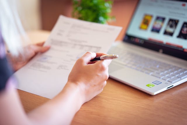 person looking at paper document near computer